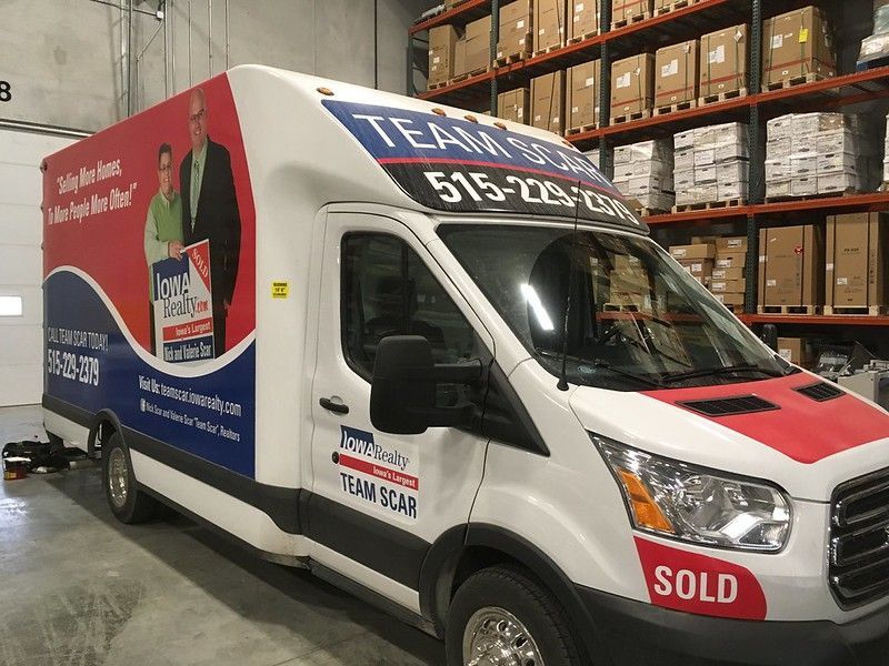 A white rental truck wrapped in Team Scar branding, parked inside a warehouse with shelves of boxes in the background.