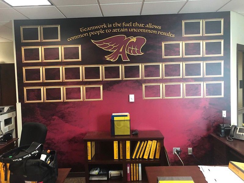 A wall display with a maroon background, gold trim, an eagle logo, an inspirational quote, and multiple empty photo frames.
