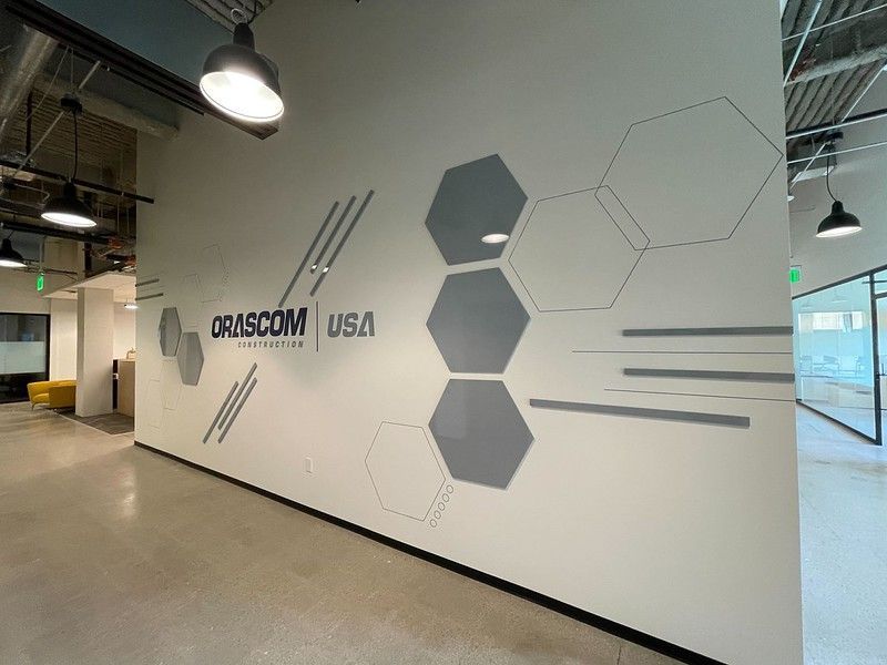 An office lobby wall featuring the Orascom USA logo alongside white and gray hexagon and line geometric wall art.