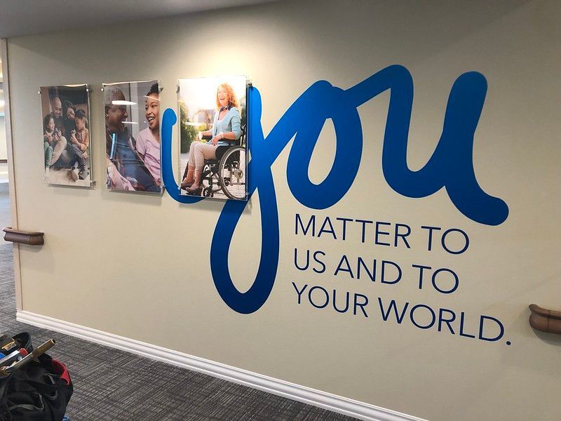 A beige wall displays three photos of diverse people and the large blue text, 