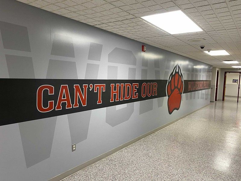 A school hallway with a grey wall featuring a black stripe reading 
