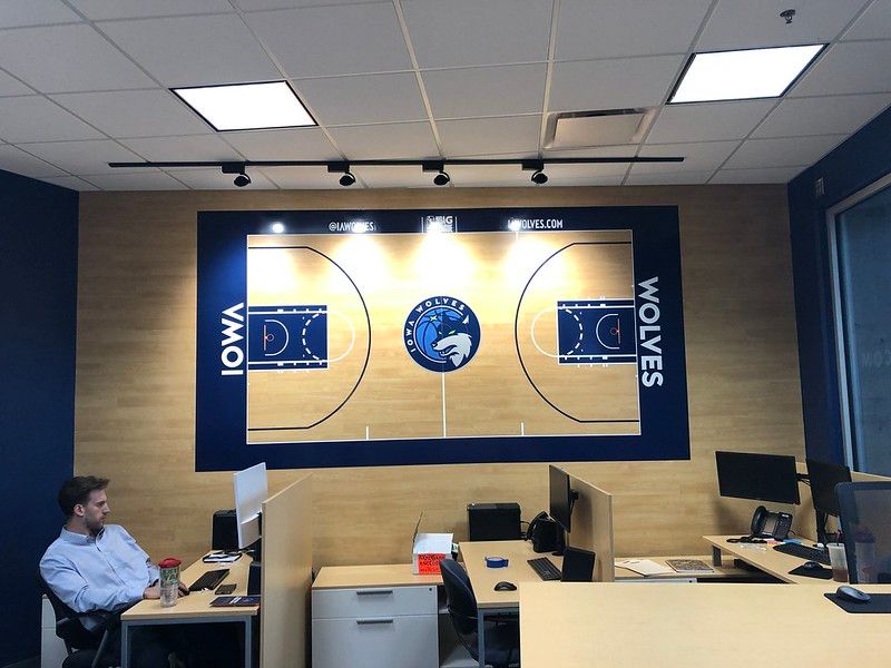 An office with cubicles featuring a large wall mural of the Iowa Wolves basketball court and team logo.