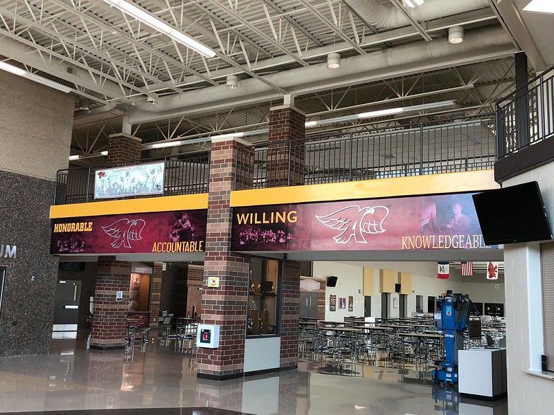 A wide-angle view of a school cafeteria with a yellow banner displaying school values like 