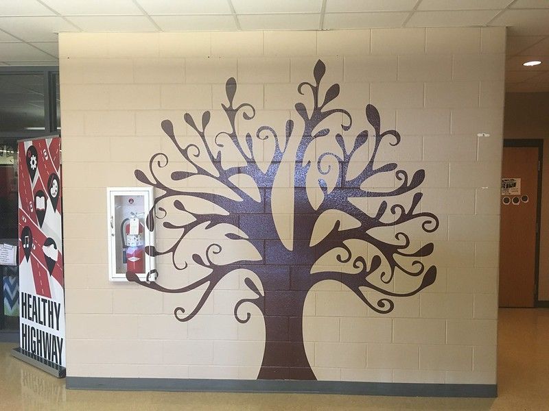 A large, dark brown stylized tree mural painted on a tan cinder block wall next to a recessed fire extinguisher cabinet.