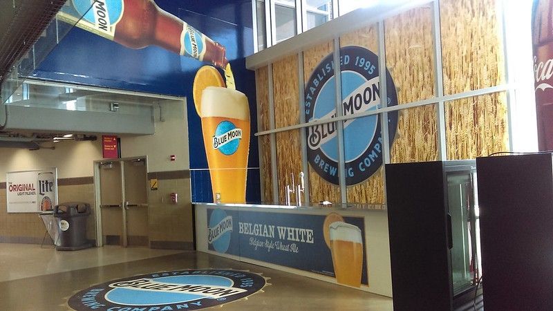 Blue Moon Brewing Company concession stand with a large 3D beer glass display and logo signage inside a stadium.