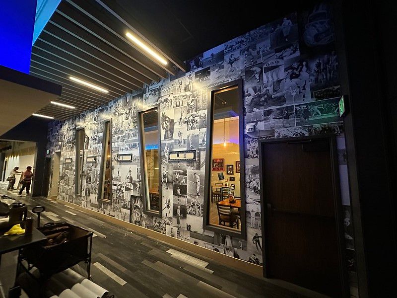 A hallway wall covered in black-and-white collage photos with vertical mirrors, recessed lighting, and a closed door.