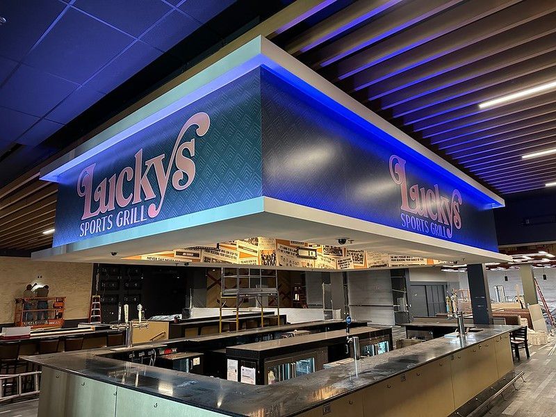 A Lucky’s Sports Grill bar with a prominent, illuminated blue sign and dark countertops in an indoor space.