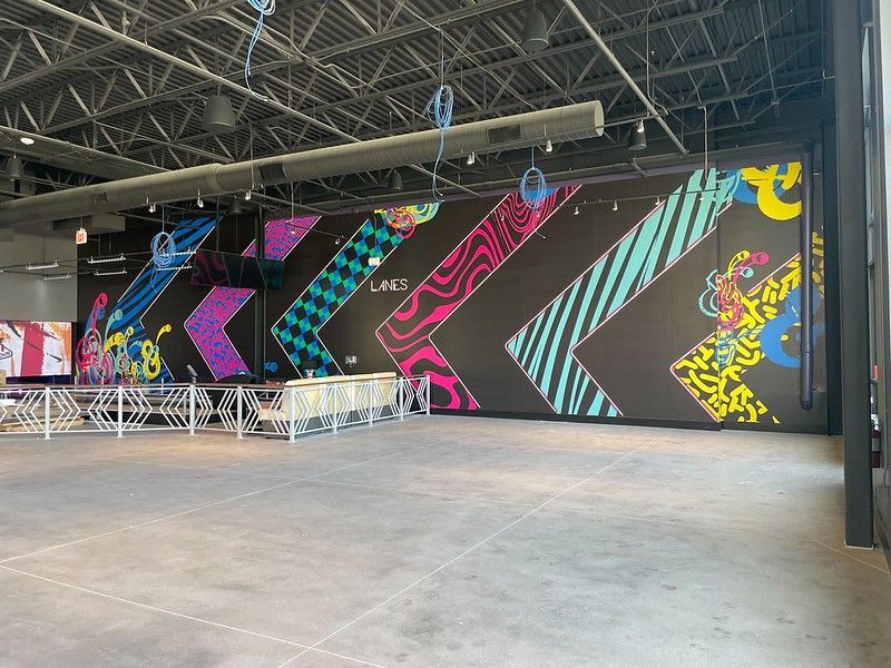 A large, open indoor space with a black wall decorated by colorful, neon-patterned chevron designs and murals.
