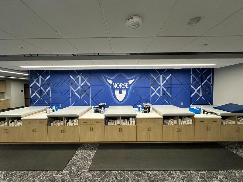 A row of treatment tables in a sports training room with a blue wall featuring a Norse logo.