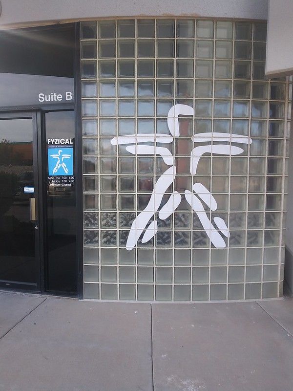 A white, abstract human-shaped decal on a glass block wall next to a glass door marked 