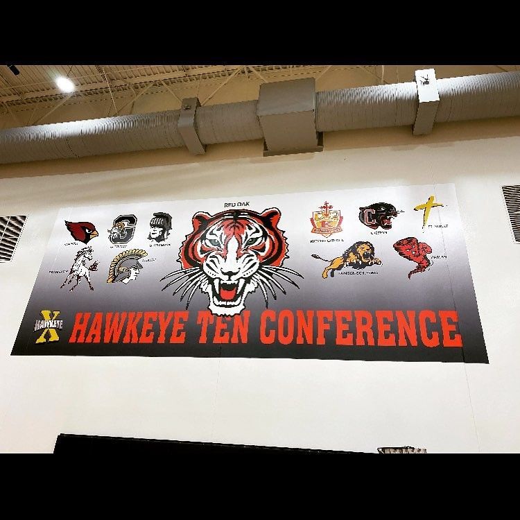 A banner on a wall displaying the Hawkeye Ten Conference logo, a tiger mascot, and logos for ten school teams.