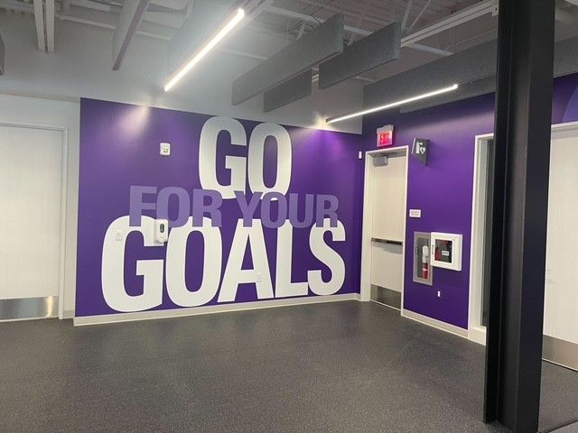 A purple wall in a gym features the white, bold text 