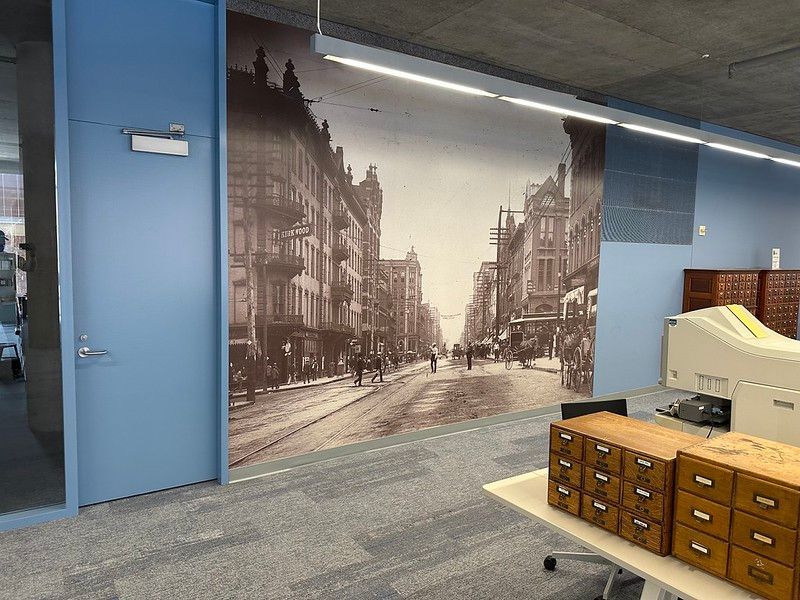 A wall-sized historic sepia-toned mural of a city street inside an office with blue doors and wooden card catalogs.