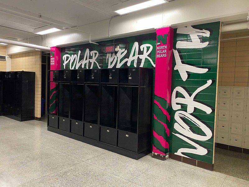 A row of black lockers against a green and pink wall mural with the words 