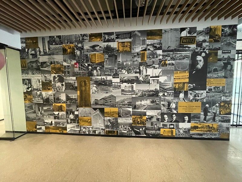 Large wall mural featuring a collage of vintage black-and-white photos with yellow accents in a brightly lit hallway.