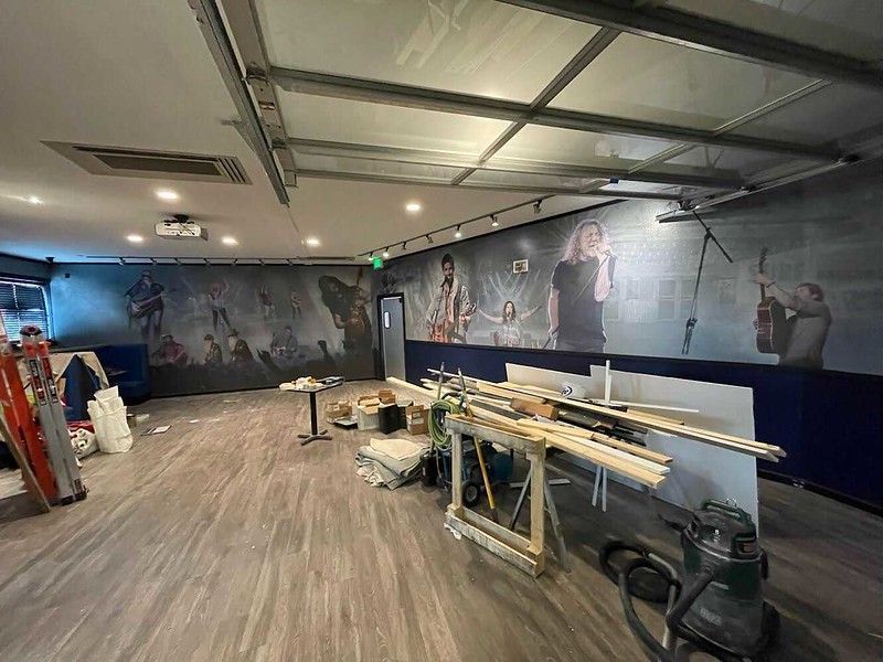 A room under construction features a long wall mural depicting music concert scenes, wood-look flooring, and work tools.