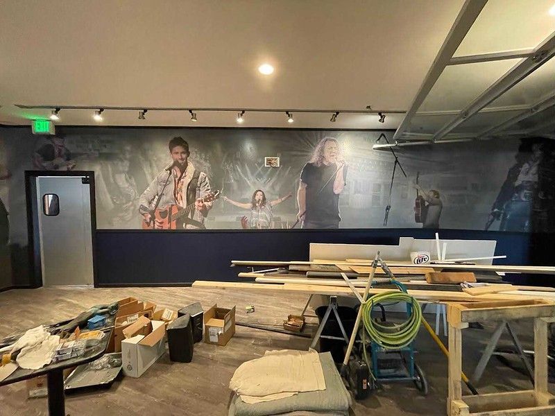 A large mural of a band performing on stage in a room under construction, with building materials scattered throughout.