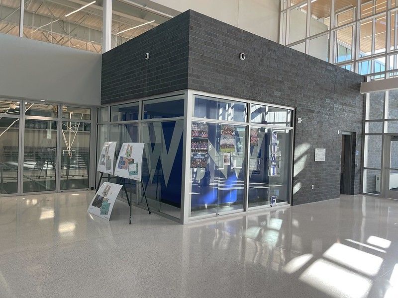 A modern building interior featuring a dark brick-walled office enclosure with glass windows and posters on display.