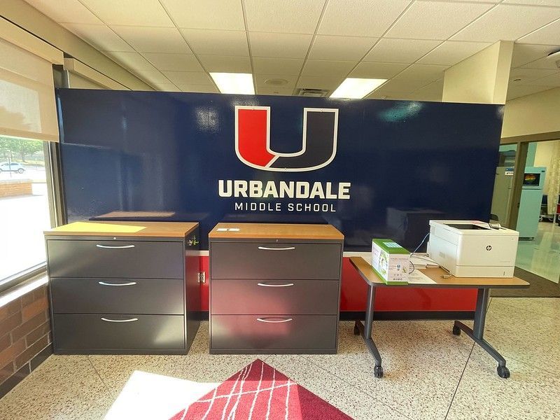 Urbandale Middle School logo on a dark blue wall behind two gray filing cabinets and a small table with a printer.