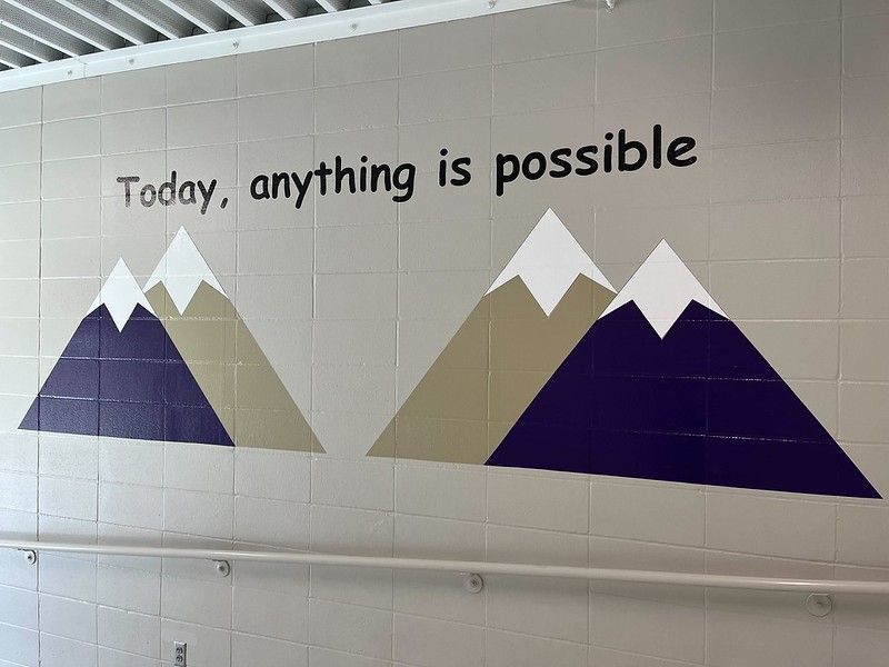 A painted wall mural featuring two mountain peaks in purple and tan with white caps, under the text, 