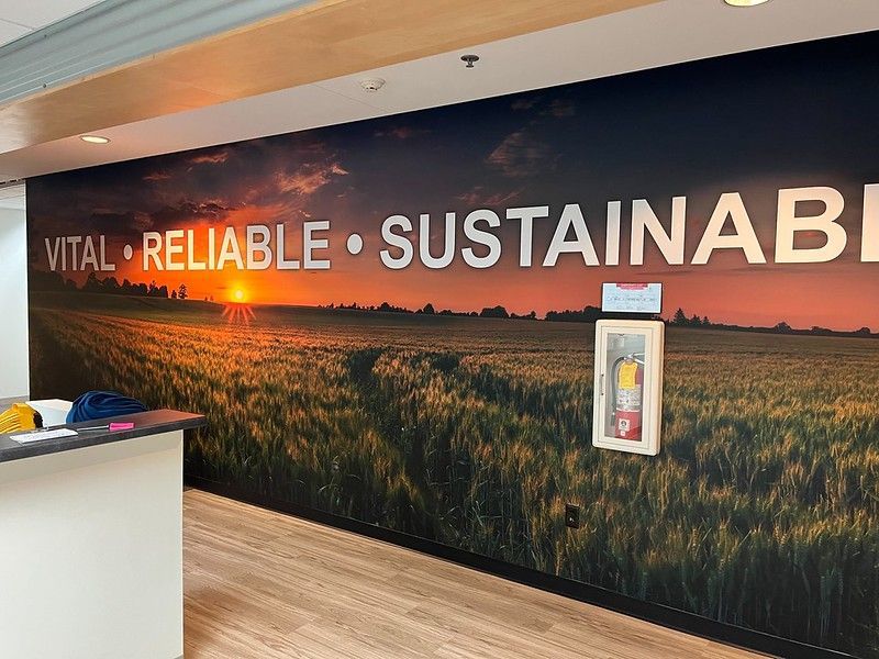 A wall mural depicting a sunset over a field with the words VITAL, RELIABLE, and SUSTAINABLE printed in white font.