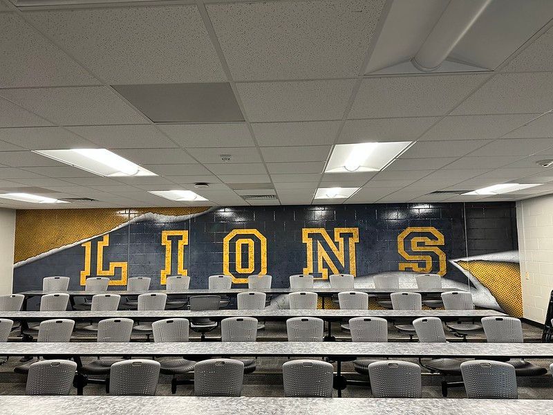 A row of gray chairs faces a table in a room with a large 