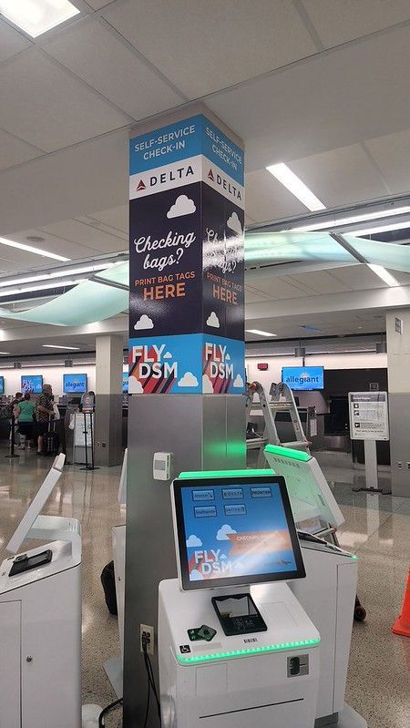 A self-service Delta kiosk stands in an airport terminal with a branded pillar behind it featuring the 