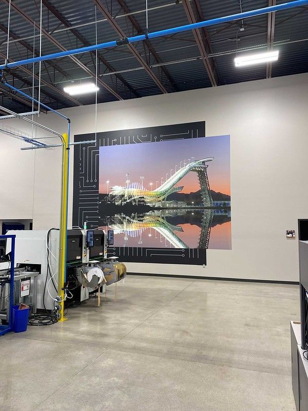 Large wall mural of a ski jump at sunset with reflection, located in a warehouse next to industrial machinery.