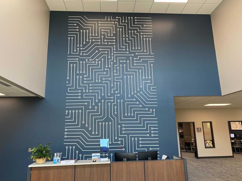 A reception desk sits before a large, dark blue feature wall painted with a white, intricate circuit board design.