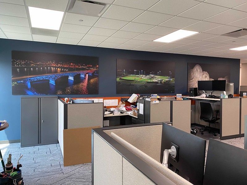 Office interior with gray cubicles and large wall-mounted night landscape photographs on a navy blue wall.