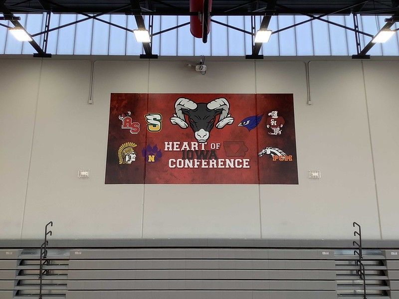 A banner for the Heart of Iowa Conference featuring a ram mascot on a red background, hanging in a school gymnasium.