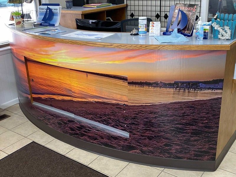 A curved reception desk featuring a sunset beach mural on its front panel, situated in a brightly lit office setting.