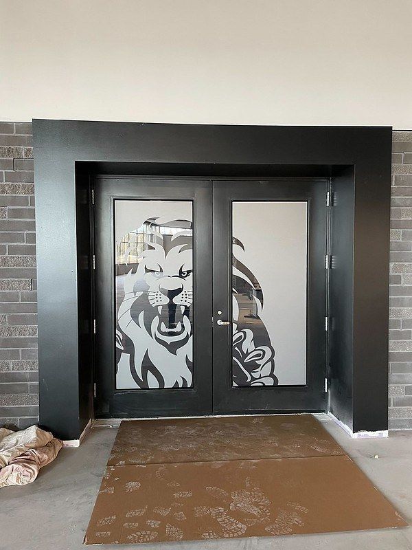 Black double doors with a frosted glass lion graphic, set in a grey brick wall.
