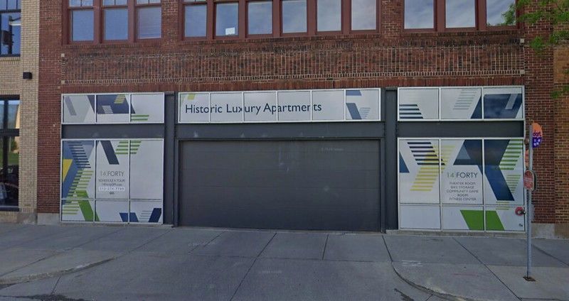 Street-level view of a brick building with windows covered by advertisements for “Historic Luxury Apartments.”