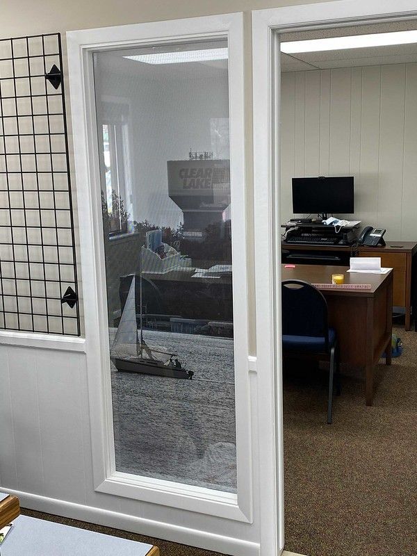 View through a glass-paned doorway into an office with a desk, computer, and a model sailboat on the floor.
