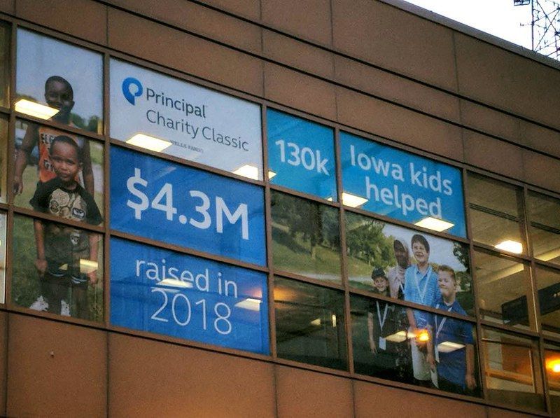 A glass building facade displaying Principal Charity Classic signage: $4.3M raised in 2018 for 130k Iowa kids helped.