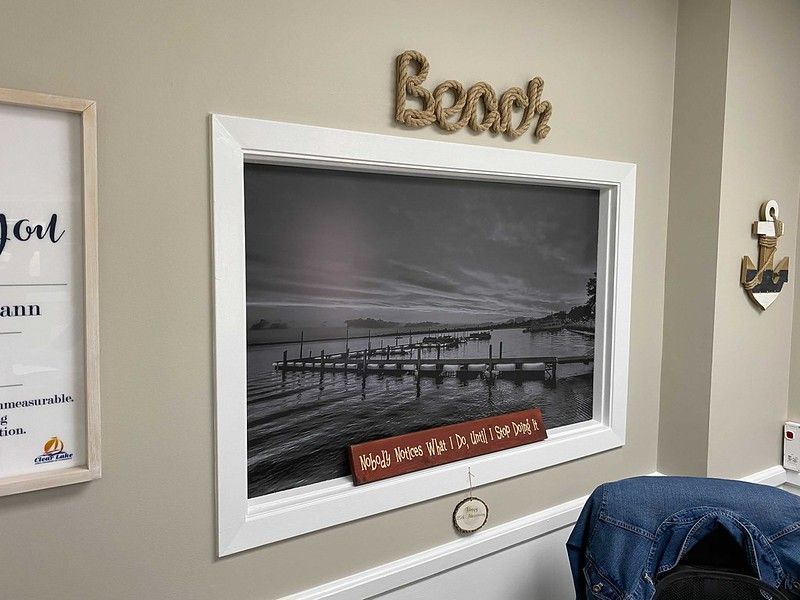 A framed, black-and-white print of a pier hangs on a beige wall, topped with a rope-style 