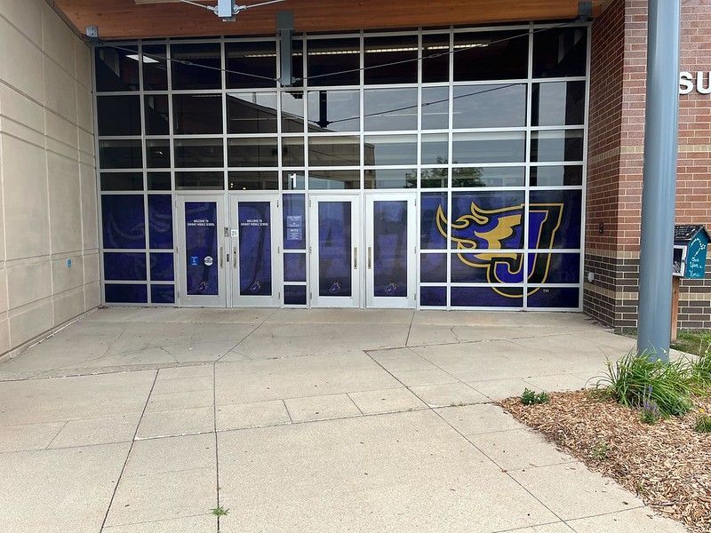 Entrance to a building with glass doors and windows featuring a purple and gold mascot logo.