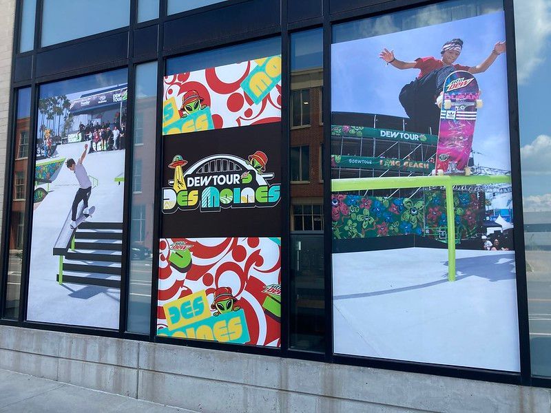 Storefront window graphics featuring skateboards, an action sports park, and a Dew Tour Des Moines event logo.