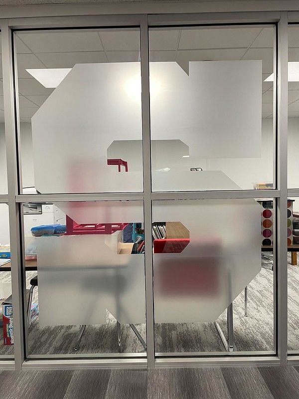 A large, frosted white graphic of the number 5, spanning across two glass office panes, obscuring a blurred desk workspace.