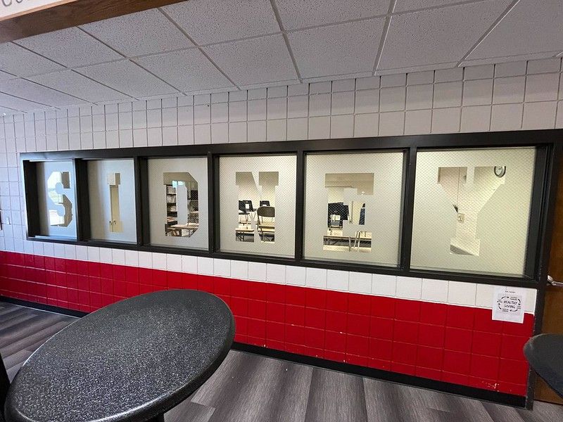 A hallway wall with red and white blocks features window panes spelling out SIDNEY in large, white, block letters.