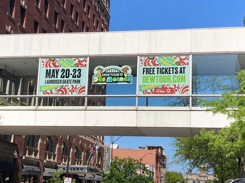 A pedestrian bridge displays Dew Tour banners promoting an event in Des Moines, May 20-23, with free tickets at dewtour.com.