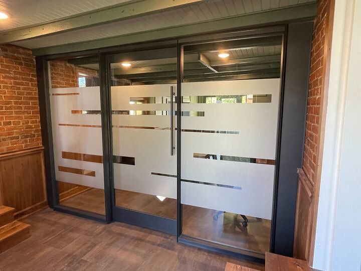Sliding glass office doors featuring a frosted horizontal stripe pattern, set within a brick wall frame.