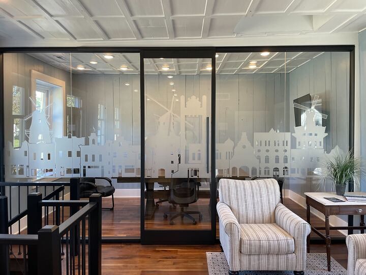 Glass office partition with etched city skyline decals, featuring a wooden table, chairs, and a striped armchair.