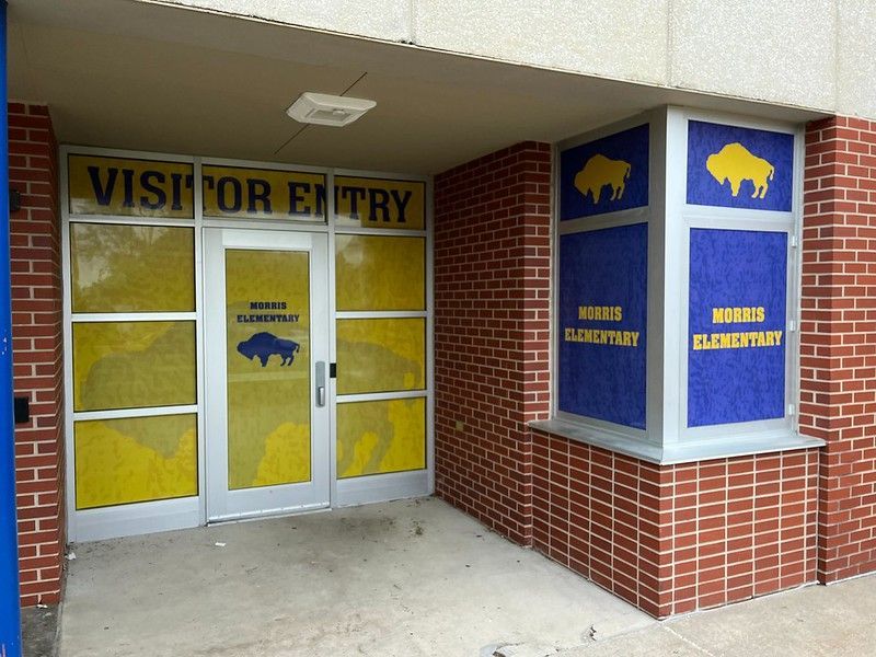 Visitor entry at Morris Elementary with yellow signage and blue corner panels, each featuring a golden bison mascot.