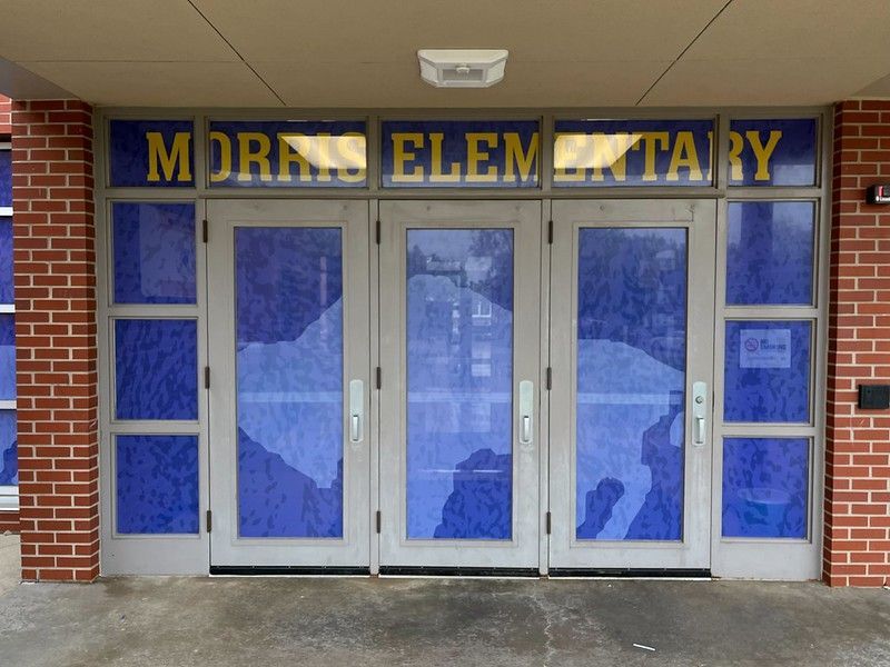 The front entrance of Morris Elementary School, featuring glass double doors with blue tinting and red brick walls.