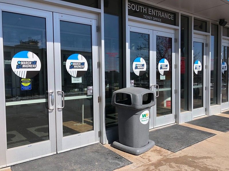 Exterior view of a building’s South Entrance, featuring glass double doors and a grey trash bin on a concrete sidewalk.