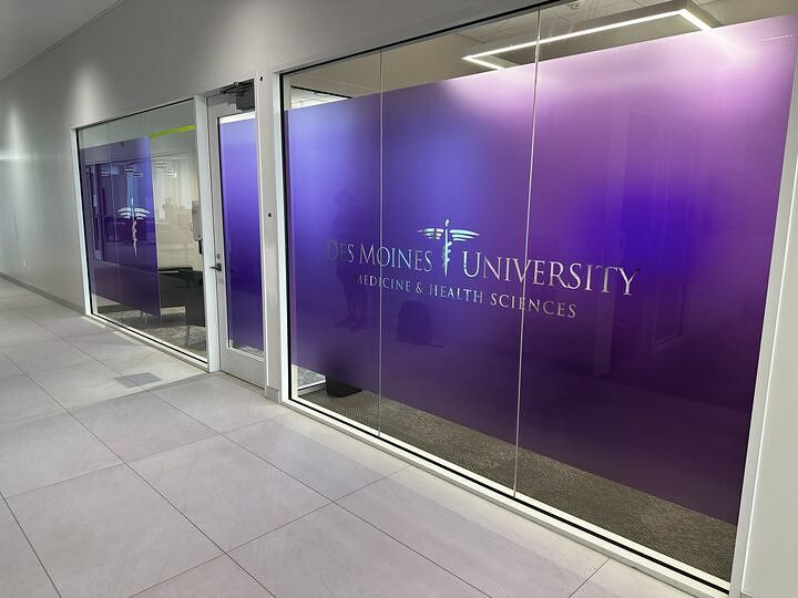 A hallway view of a Des Moines University Medicine and Health Sciences office with purple frosted glass branding.