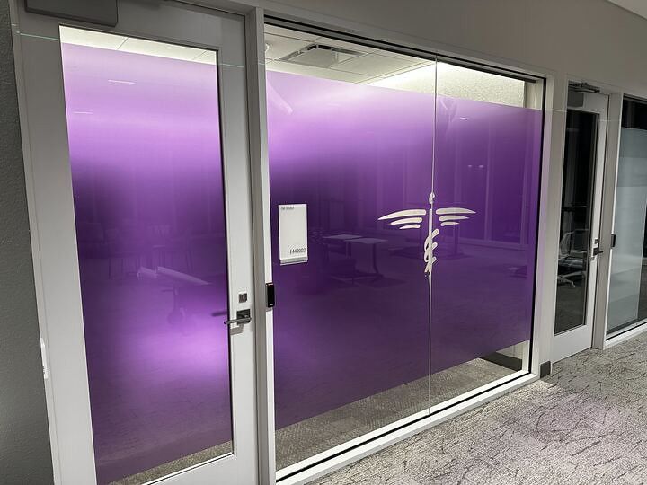 A purple frosted glass door and wall panel featuring a white medical caduceus symbol, located in a professional office.