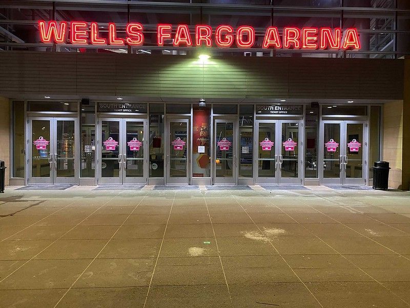 Exterior view of Wells Fargo Arena at night, featuring a glowing red sign above multiple glass entry doors.